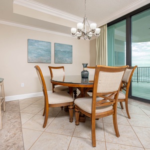 Dine at this round table surrounded by comfortable chairs, with a view through large glass doors to the balcony