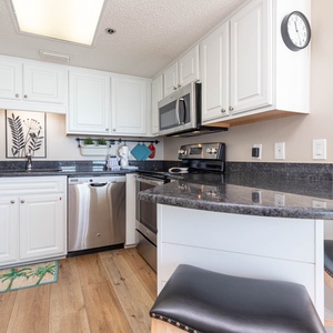 White cabinetry and sleek black countertops create a stylish, modern kitchen with a breakfast bar and seating