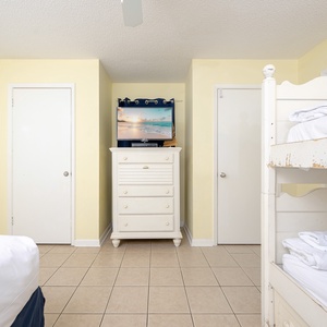 A cozy guest room features a white twin bunk bed, plus a queen bed, and a dresser with a TV, creating a cheerful atmosphere