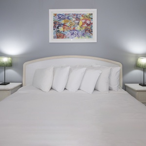 This cozy bedroom features a queen bed with crisp white linens, complemented by stylish green lamps and vibrant artwork