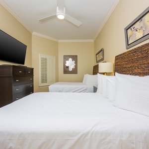 This guest bedroom features two comfortable queen beds, a flat-screen TV, and decorative art, inviting a restful stay