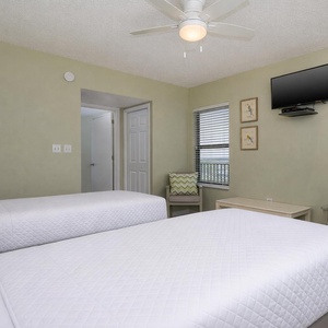 This guest bedroom features two beds, a TV, and a cozy seating area with a view of the vibrant outdoors