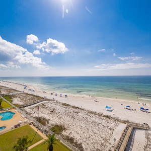 Sunlight dances across the calm coast as you watch families enjoy the inviting beach below