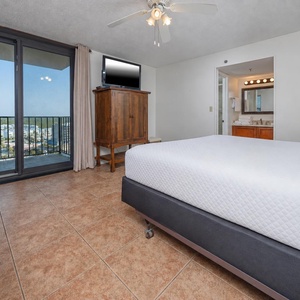 Master bedroom featuring a king bed, flat-screen TV, and a stunning balcony view of the vibrant coastal landscape