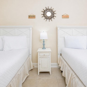 Inviting guest bedroom featuring two plush queen beds, a stylish lamp, and charming coastal decor