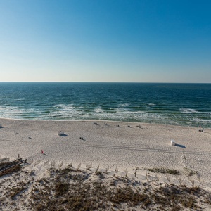A serene view of the beach front showcases soft white sand and gentle waves under a clear blue sky