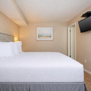 This guest bedroom features a cozy queen bed, a mounted TV, and soft lighting for a relaxing stay