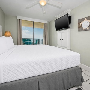 A cozy master bedroom features a plush king bed, flat-screen TV, and a balcony view with seating overlooking the beach