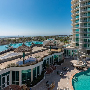 This view showcases a vibrant pool area with a waterslide, palm trees, and a serene view, perfect for relaxation