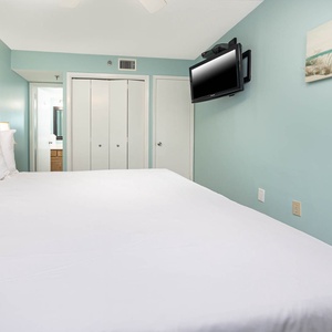 Spacious geust bedroom features a large white king bed, a mounted TV, and soft blue walls, creating a tranquil atmosphere