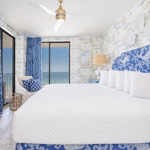 Master bedroom featuring a king bed, beach-front balcony, and vibrant blue decor for a relaxing getaway