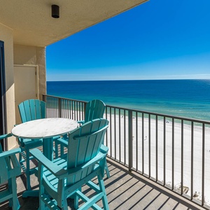 Balcony features turquoise chairs and a round table, offering a serene view of the tranquil blue waters and white sand below