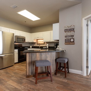 Modern kitchen features a breakfast bar with two stools, sleek countertops, and a welcoming coastal-themed decor
