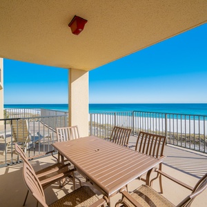 The spacious extended balcony features a dining table with seating, offering direct views of the tranquil beach