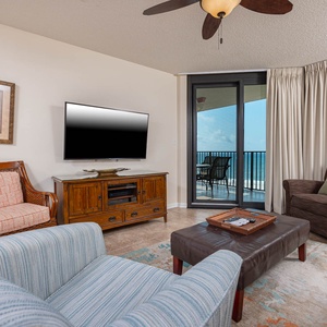 Living area features a plush sofa with queen sleeper, accent chairs, and a view of the beach from the balcony