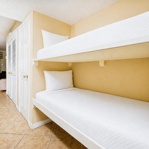 This cozy bunk area features two neatly made beds and offers a glimpse of the inviting beach view beyond