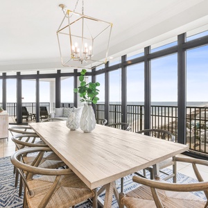 This dining area features a light wood table surrounded by stylish chairs, with stunning beach views through large windows