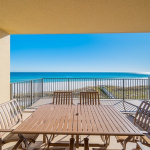Extended balcony features a dining table with seating and offers a breathtaking view of the turquoise waters and beach