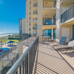 This balcony features lounge chairs and offers a direct view of the beach and pool area under a bright blue sky