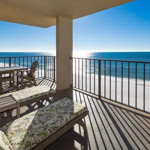 The balcony features two lounge chairs and a dining table, offering a serene view of the tranquil beachfront