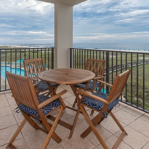 Wooden table with navy-accented chairs on the balcony offers a serene view of the beach and pool area, perfect for relaxation