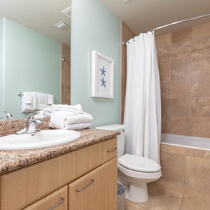 This bathroom features a stylish granite countertop, a relaxing tub-shower combo, and fresh towels, creating a serene retreat