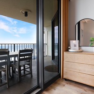 A stylish wooden dresser with a mirror and plant complements the view of the balcony with outdoor seating