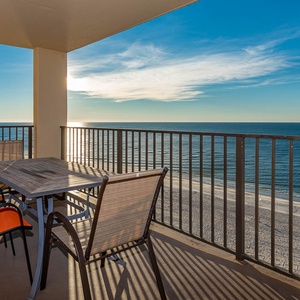 Enjoy a relaxing moment on the balcony with a table and orange-accented chairs overlooking the tranquil beachfront
