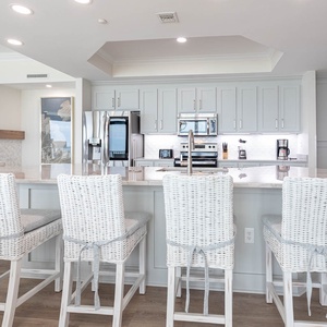 The modern kitchen features stainless appliances, a coffee maker, and a spacious island with stylish bar stools