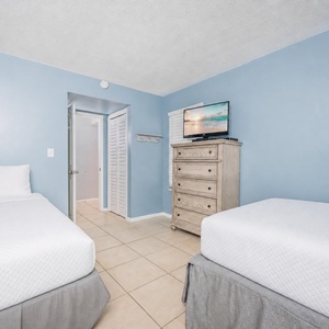 Guest bedroom featuring two comfortable beds, a full and a twin, TV, and calming blue walls with tiled flooring