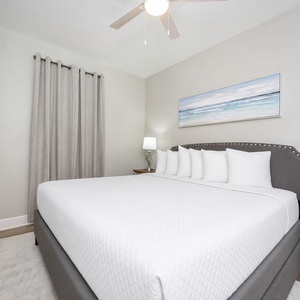 Cozy guest bedroom features a plush king bed with decorative pillows, a stylish lamp, and a wall-mounted TV for entertainment