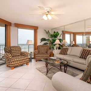 The living area features patterned armchairs, a cozy sofa with queen sleeper, and a view of the beach