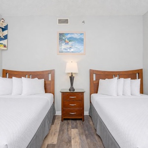 The guest bedroom features two neatly made double beds with plush white linens, a bedside table, and cheerful nautical decor