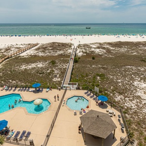 View of the inviting pool area with lounge chairs and umbrellas, leading to the beautiful beach and sparkling gulf waters