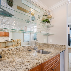 Wet bar area features granite countertops, a blender, ice-maker, and a view of the cozy living area with beach vibes