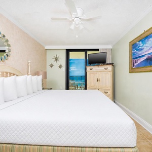 Brightly decorated master bedroom featuring a king bed, a TV, and the balcony door leading to a view of the beach front