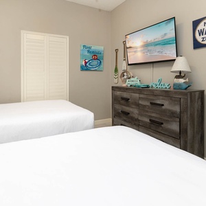 Welcoming guest bedroom featuring two comfortable double beds, beach-themed decor, and a TV for your entertainment
