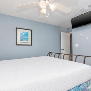 This bedroom features a cozy bed, a mounted TV, and calming blue walls, creating a relaxing retreat for guests