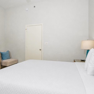 Rest in this guest bedroom featuring a large queen bed, a TV, and a cozy chair for relaxing after a day of adventure