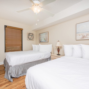 Brightly decorated bedroom featuring two double beds, a flat-screen TV, and coastal artwork, creating a relaxing atmosphere