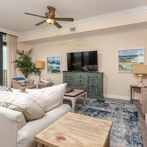 This inviting living area features a large TV, plush seating, and a beautiful beachfront view framed by expansive windows