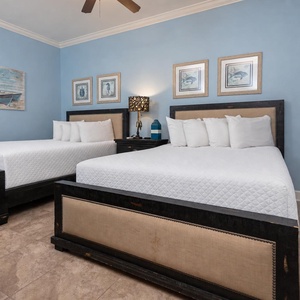 This guest bedroom features two queen beds with soft linens, a calming blue wall, and nautical decor for a relaxing stay