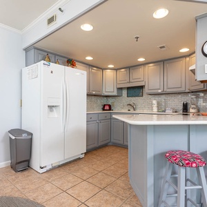 The well-equipped kitchen features light gray cabinetry, white appliances, and colorful bar stools at the counter