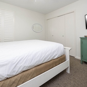Cozy guest bedroom featuring a plush queen bed, green dresser, and a wall-mounted TV for your entertainment