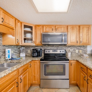 Prepare meals in this inviting kitchen featuring granite countertops, stainless appliances, and a view of the beach