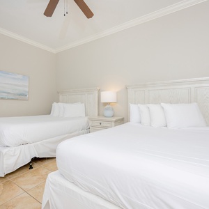 Calming guest bedroom featuring two cozy queen beds, elegant white linens, and a soothing coastal painting