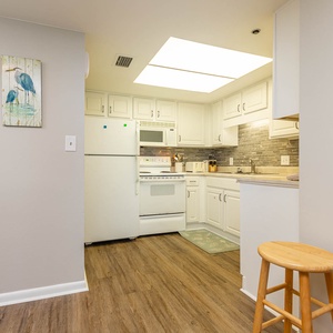 Bright and inviting kitchen featuring white cabinetry, white appliances, and a cozy breakfast bar with wooden stools