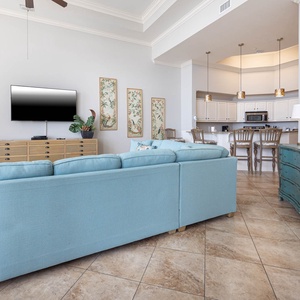 The living space features a cozy blue sofa, a large TV, and a stylish kitchen with bright decor and inviting seating