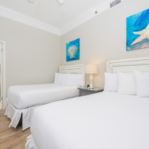 Guest bedroom featuring two double beds with white linens, coastal artwork, and a bedside lamp, creating a serene atmosphere
