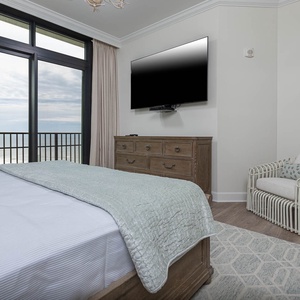 The master bedroom features a cozy king bed, a large TV, and beachfront views from the balcony door